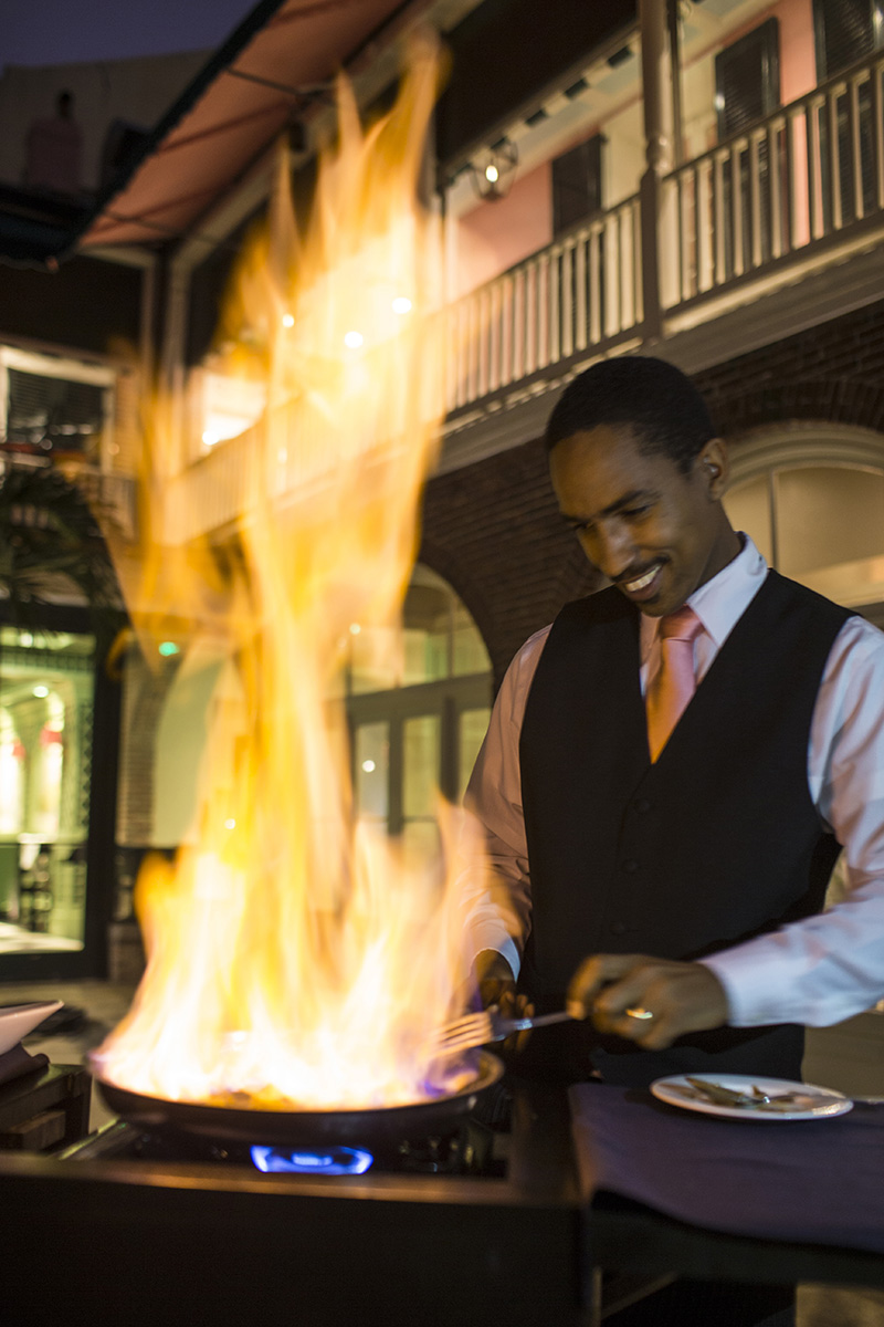 A pan on a stove lights in fire with a server next to it