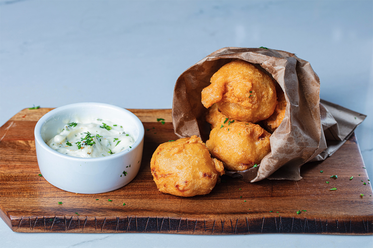 Beignets spilling out of a bag with a dipping sauce on the side in a white ramekin