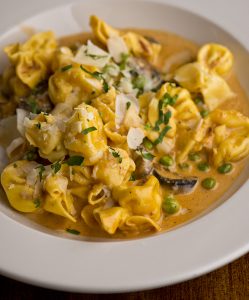 Four cheese-stuffed pasta in a pink sauce with peas, mushrooms, and prosciutto