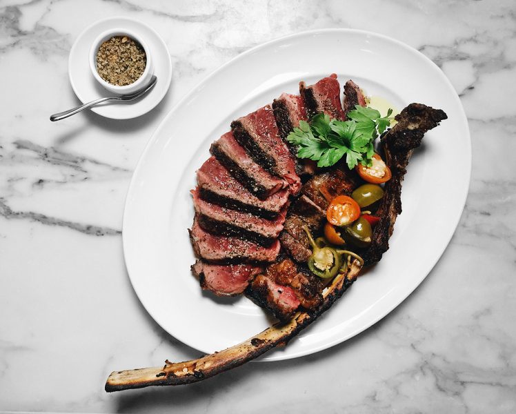 A medium-rare tomahawk steak splayed on a white plate