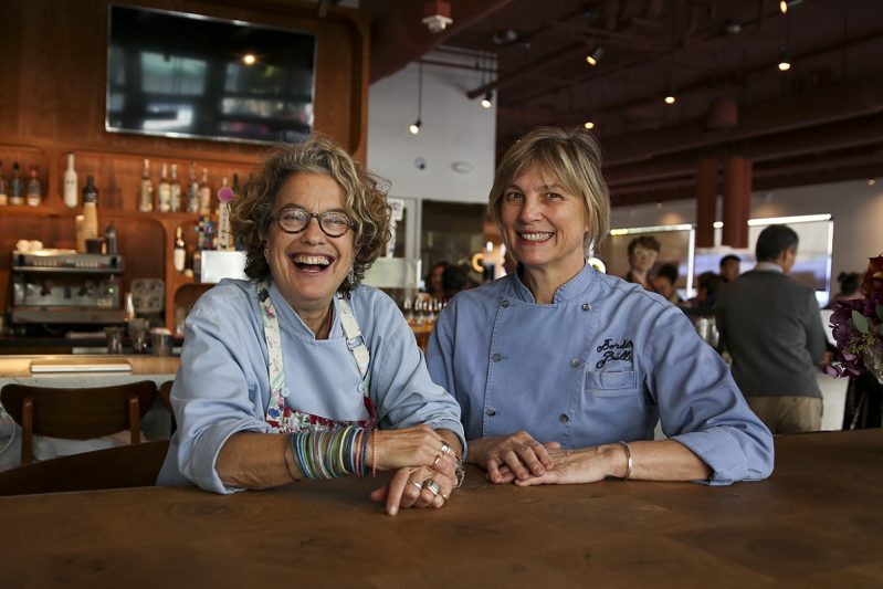 Susan Feniger and Mary Sue Milliken smile at a table