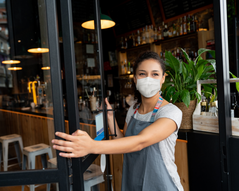 A masked server opens the door of a restaurant
