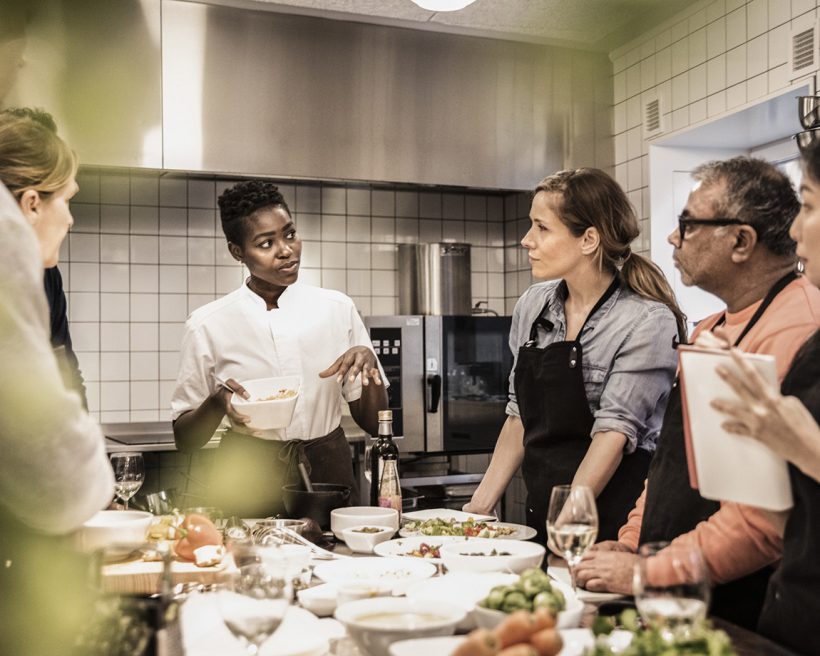 A Black chef demonstrates how to make a dish to her employees