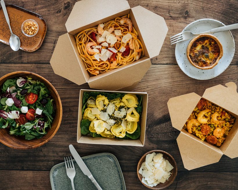 Flat lay view of takeaway meals on dinner table - with pasta, vegetable salad and seafood risotto.