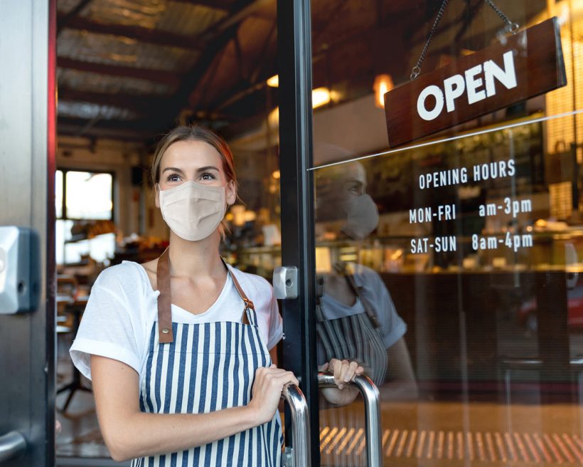 Happy business owner opening the door at a cafe wearing a face mask