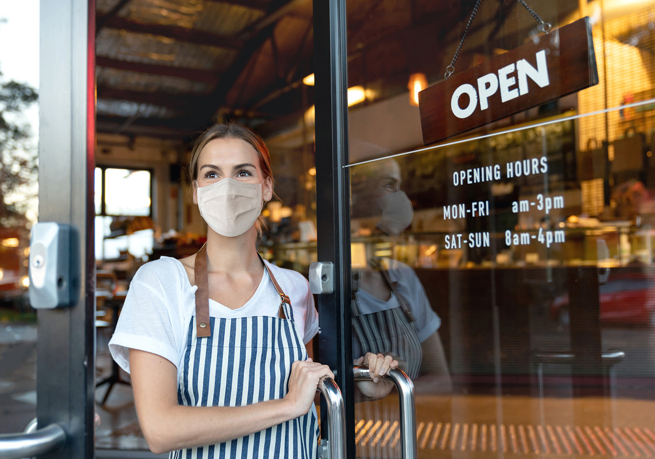 Happy business owner opening the door at a cafe wearing a face mask
