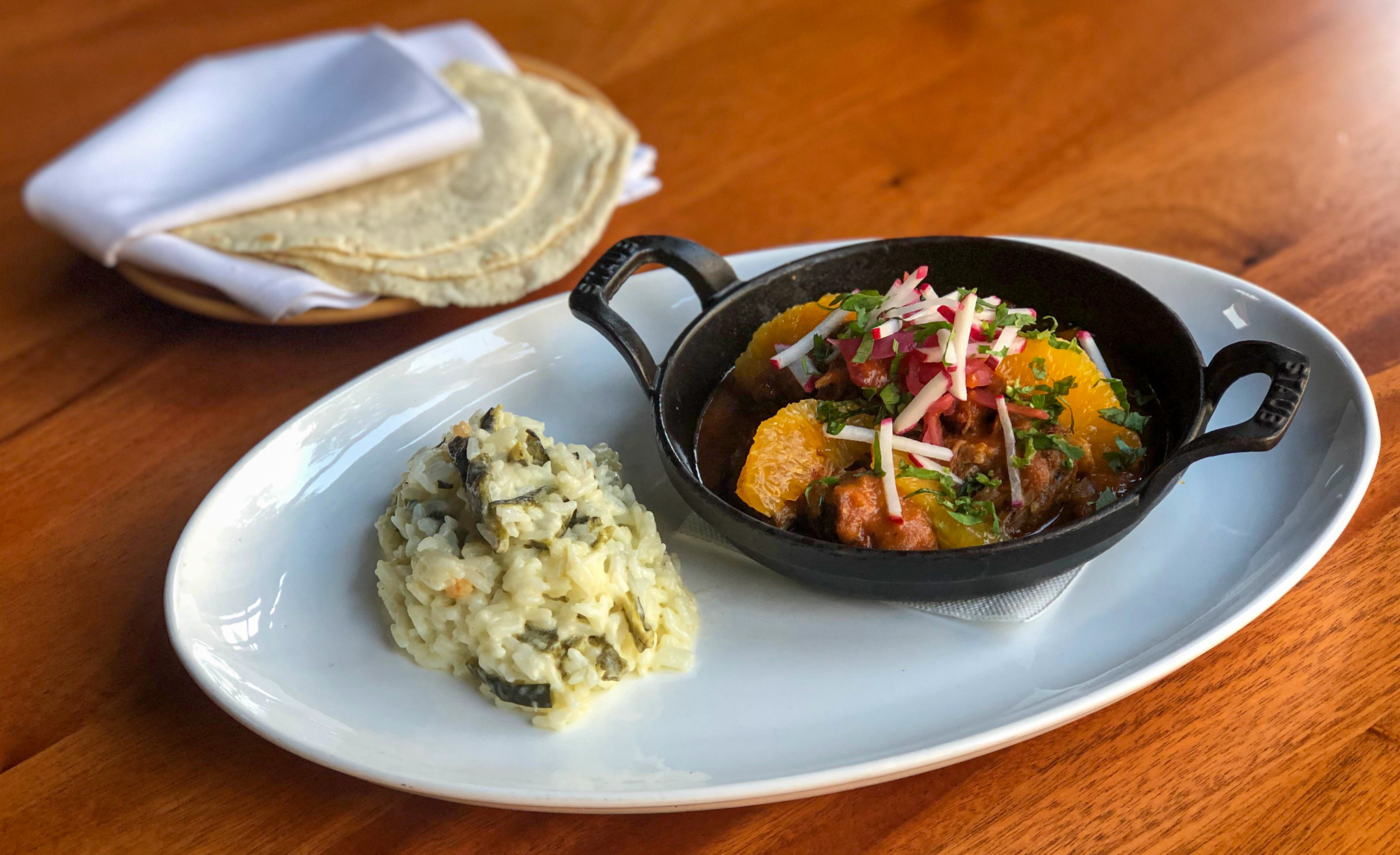 Pork in a small skillet on a plate with rice and tortillas