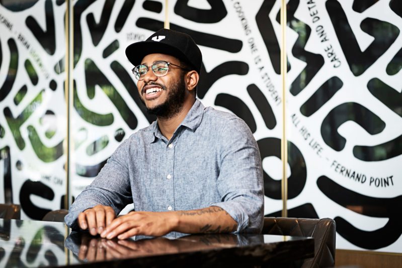 Kwame Onwuachie sits a table smiling