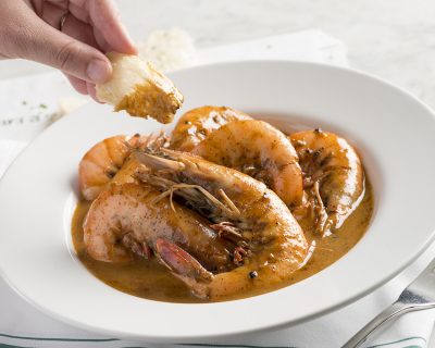 A hand dipping bread into barbecue shrimp