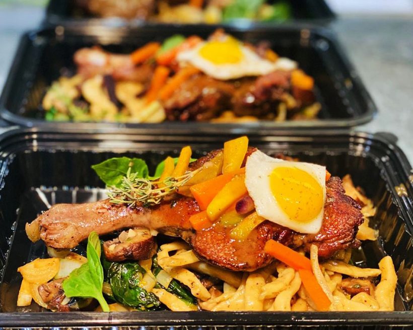 Duck confit in a takeout container with an egg on top