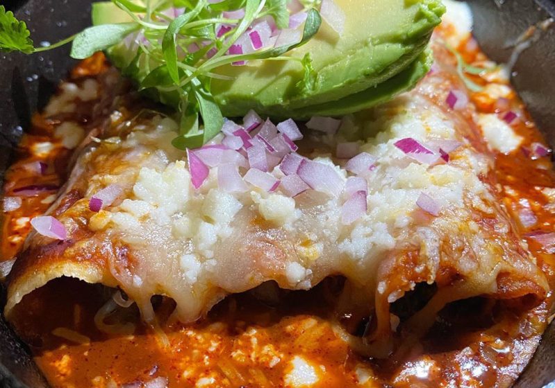 Enchiladas topped with cheese and avocado