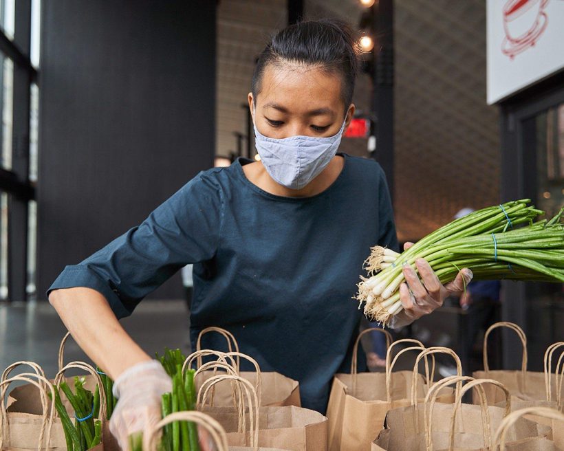 A masked chef packs bags with scallions