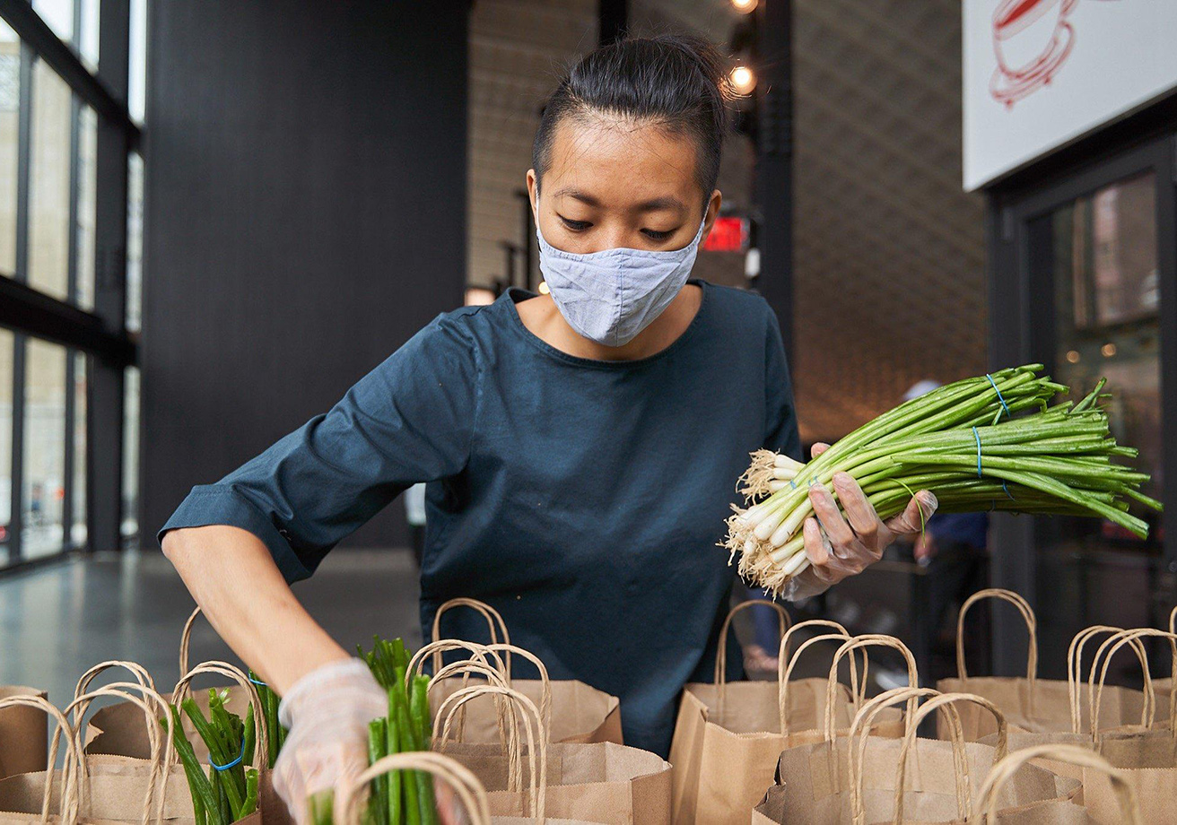 A masked chef packs bags with scallions