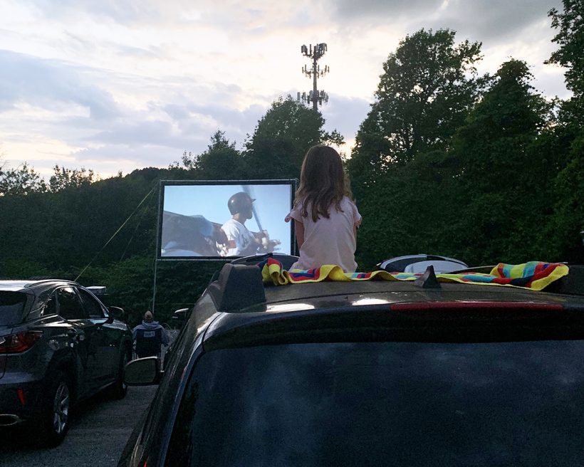 A child sits on top of a car at a drive-in movie