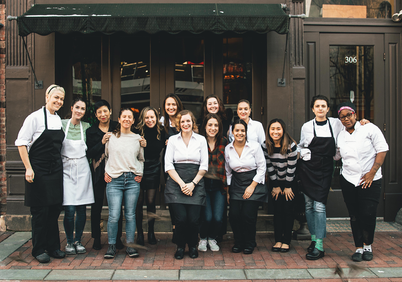 A group of restaurant workers poses in front of a restaurant