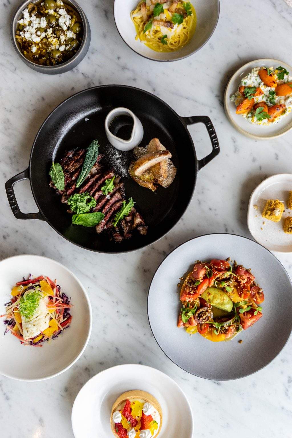 A wagyu ribeye in a black bowl surrounded by smaller vegetable sides at Arlo Grey by Kristen Kish in Austin