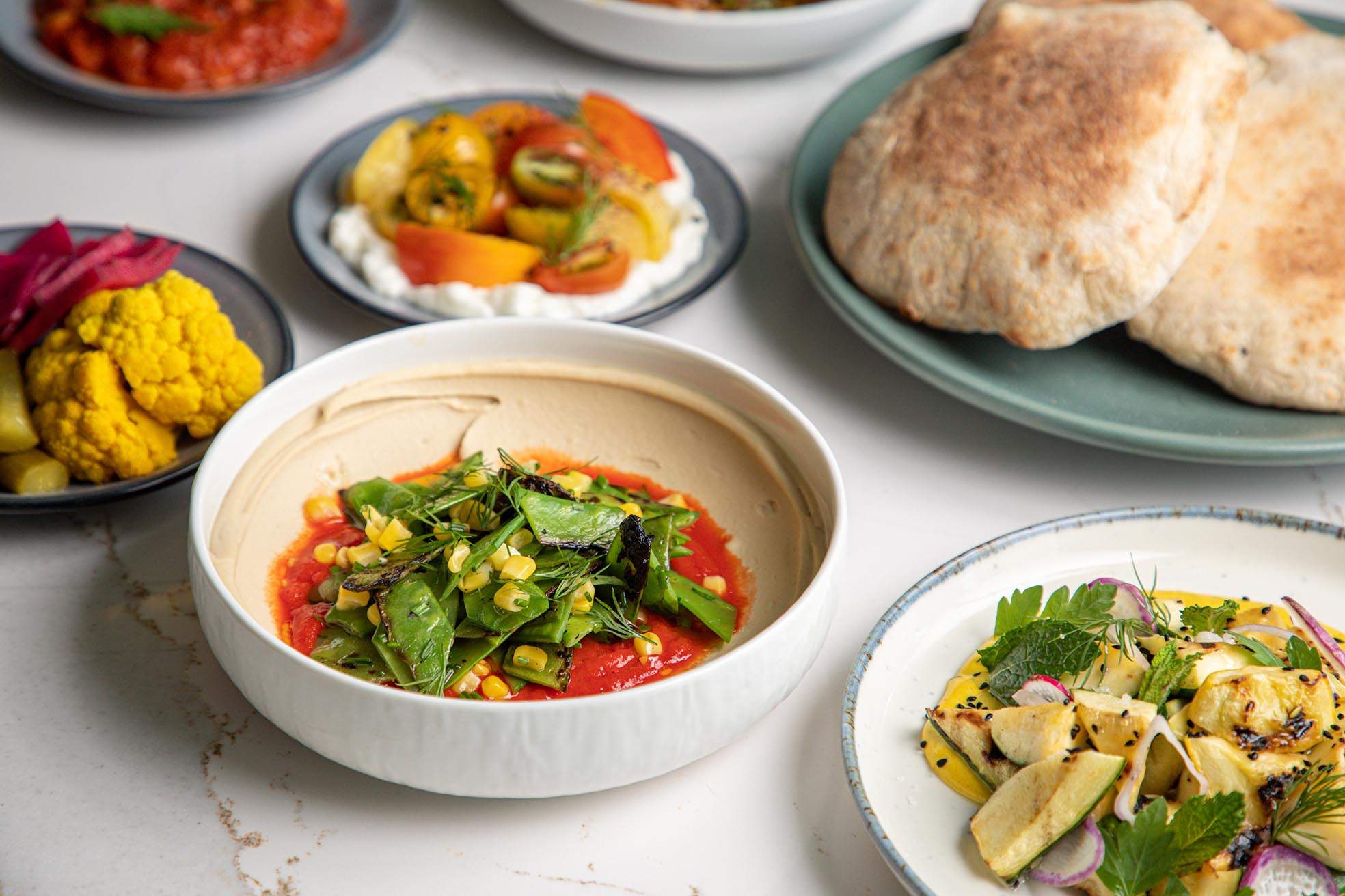 A teal dish with pita bread and bowls of assorted vegetable dips at Shaya in New Orleans