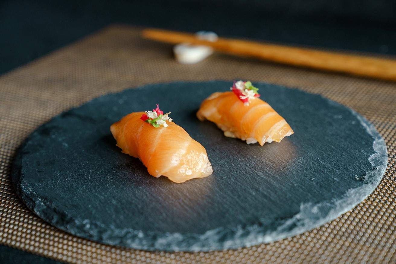 Two pieces of nigiri topped with edible flowers on a round slate dish at Yō Nashi in New Orleans