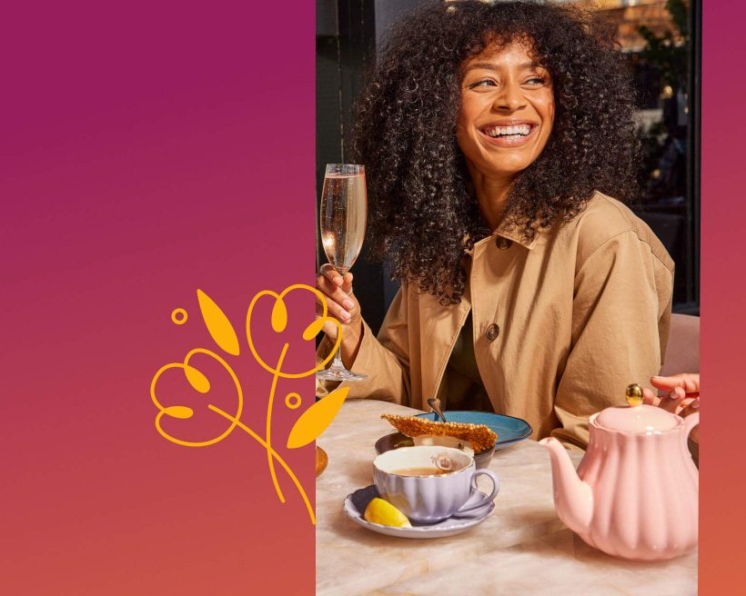 A woman is smiling at a table with tea and breakfast