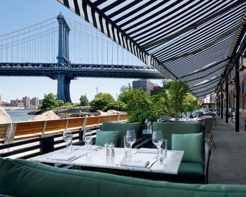 A Brooklyn Bridge view from the lounge-style seats under a black-and-white verandah at Cecconi’s Dumbo in New York City