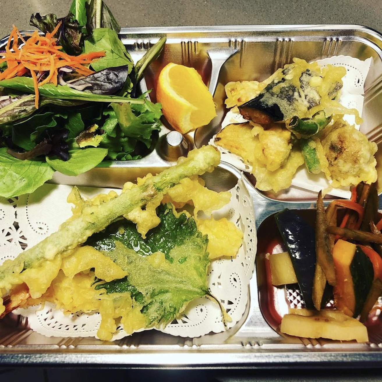 A series of tempura and cooked vegetables placed on a steel tray