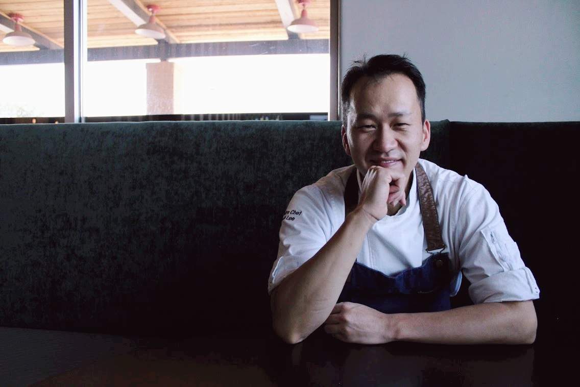 Chef Keunsik Lee sits in a white shirt and an apron on a bench.