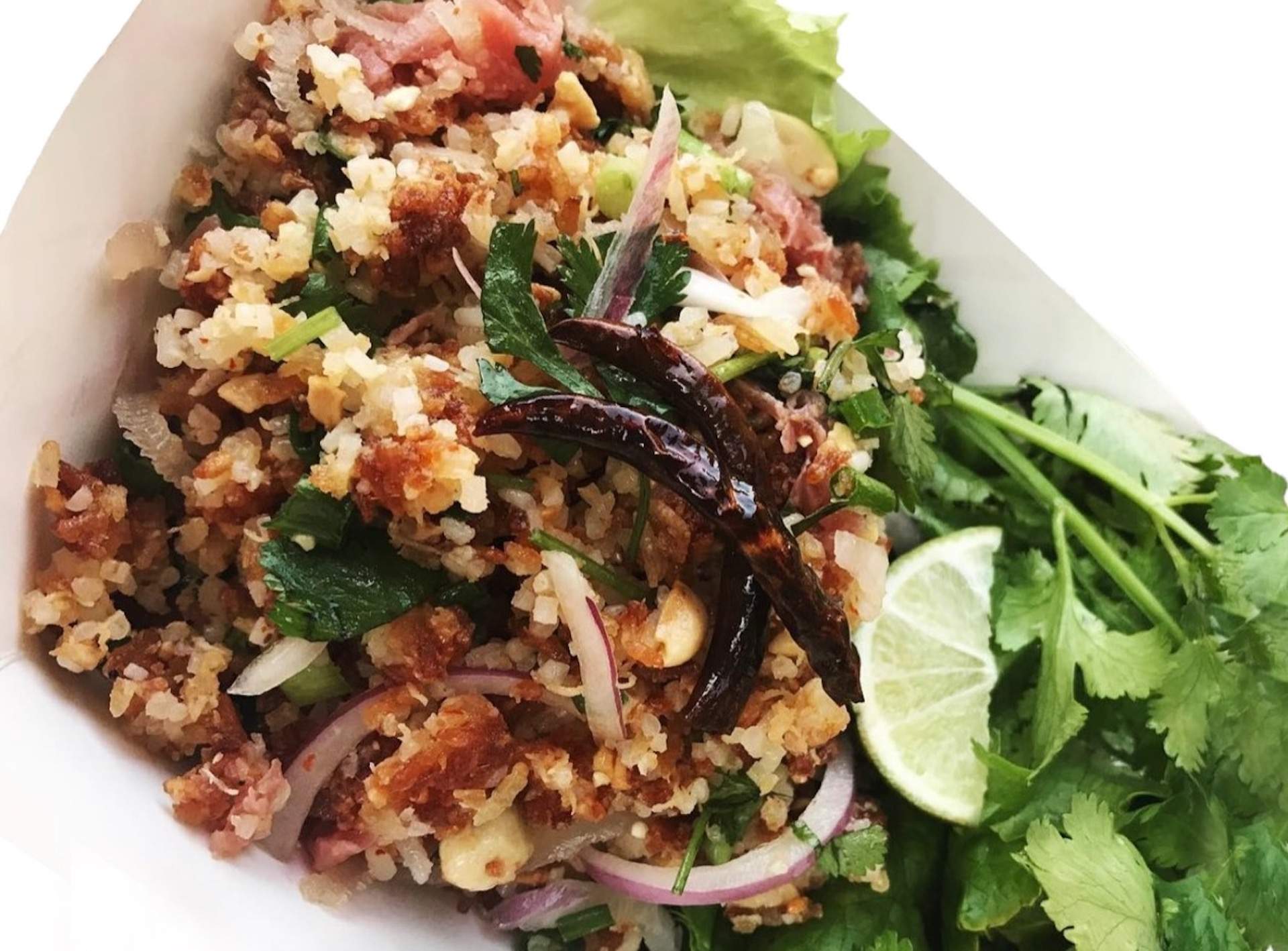 A close up of a salad called Nam Khao with herbs, meat and a lime.
