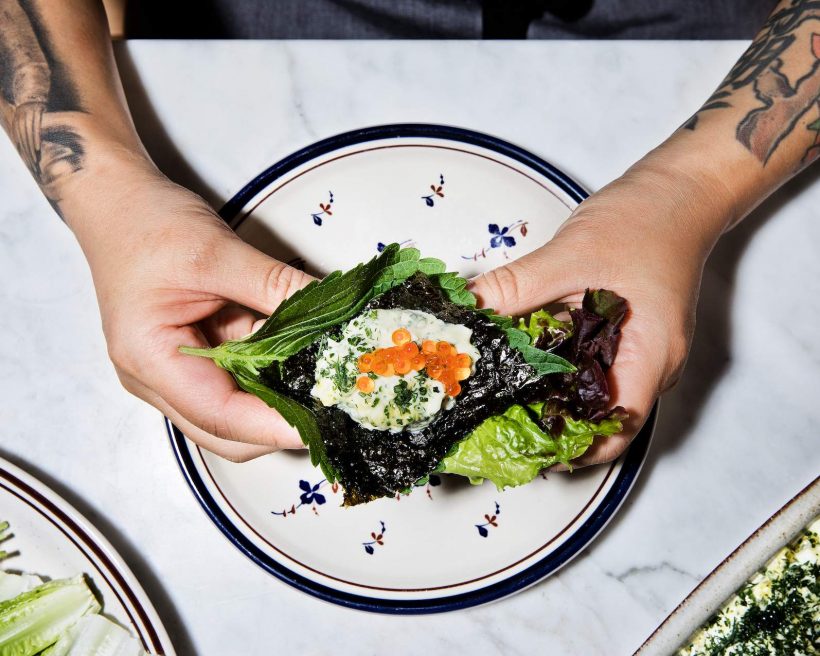 Two hands holding some egg salad with orange caviar on top sandwiched in green leaves