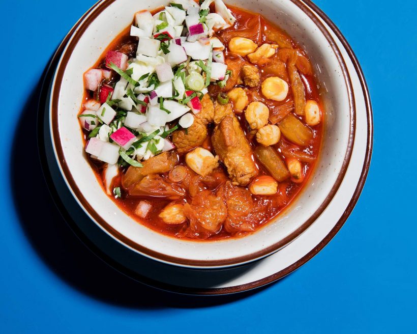 A bowl of brown food that is kimchi and pork belly posole