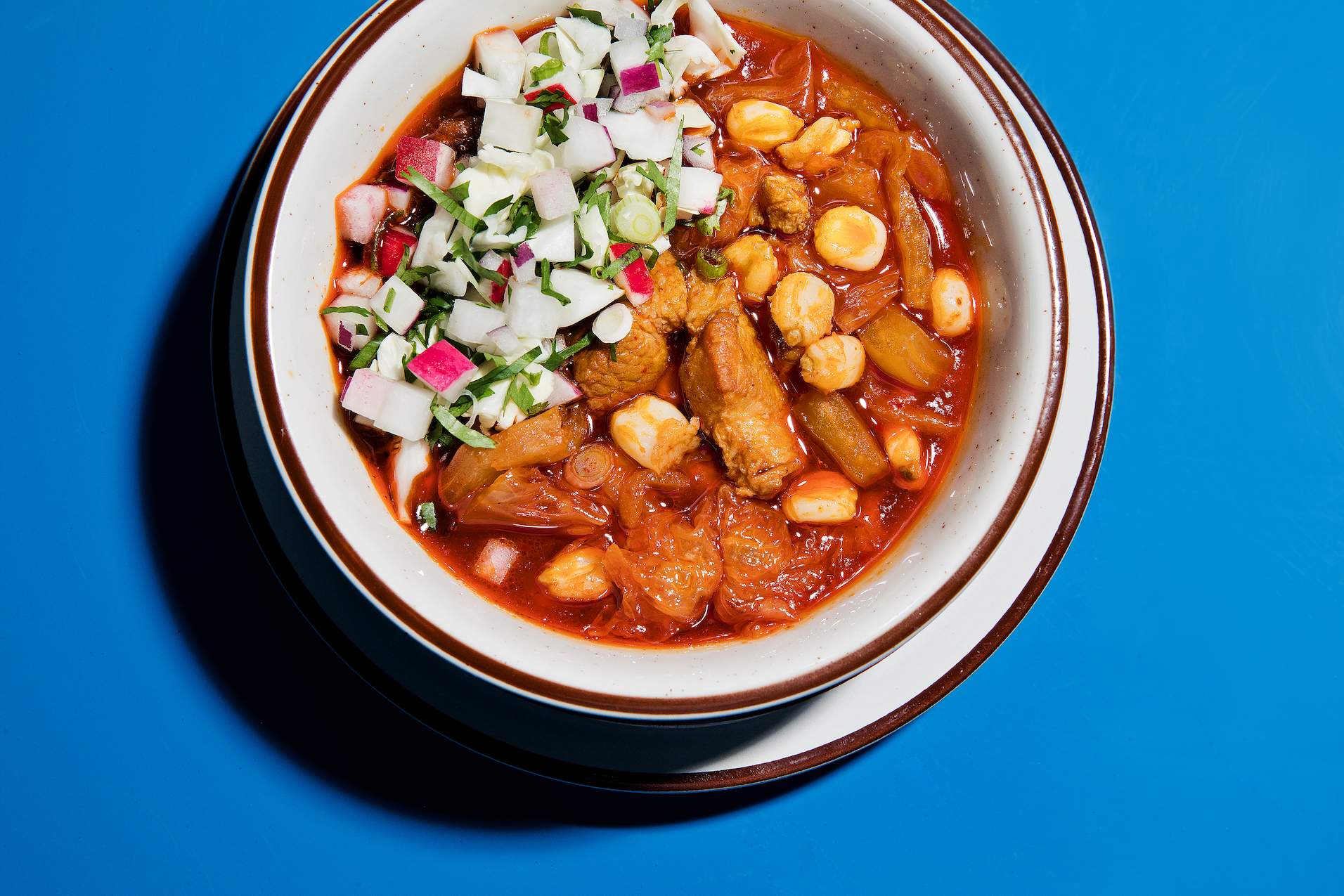 A bowl of brown food that is kimchi and pork belly posole