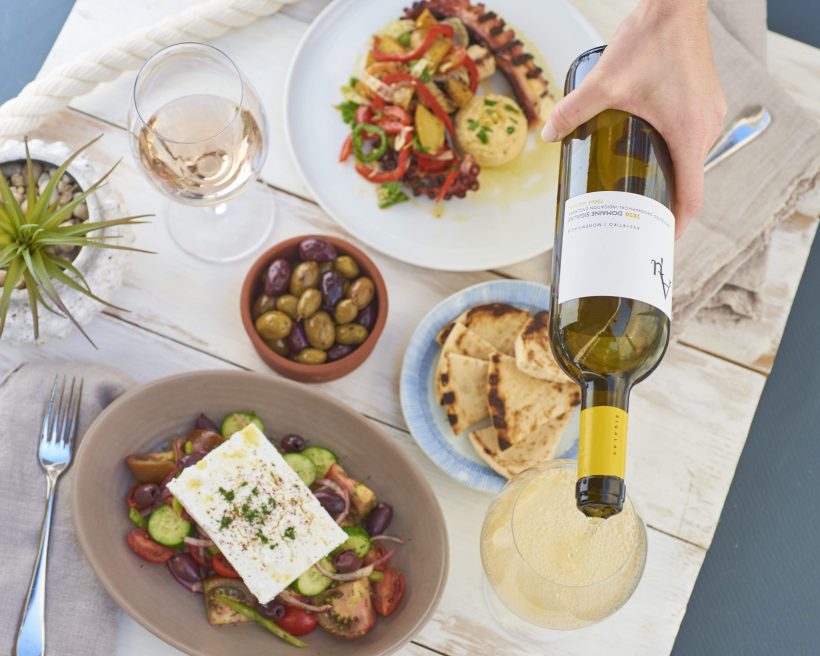 A bottle of white Greek wine, a cucumber and tomato salad topped with a slab of feta cheese, and assorted mezze plates at Calissa in the Hamptons