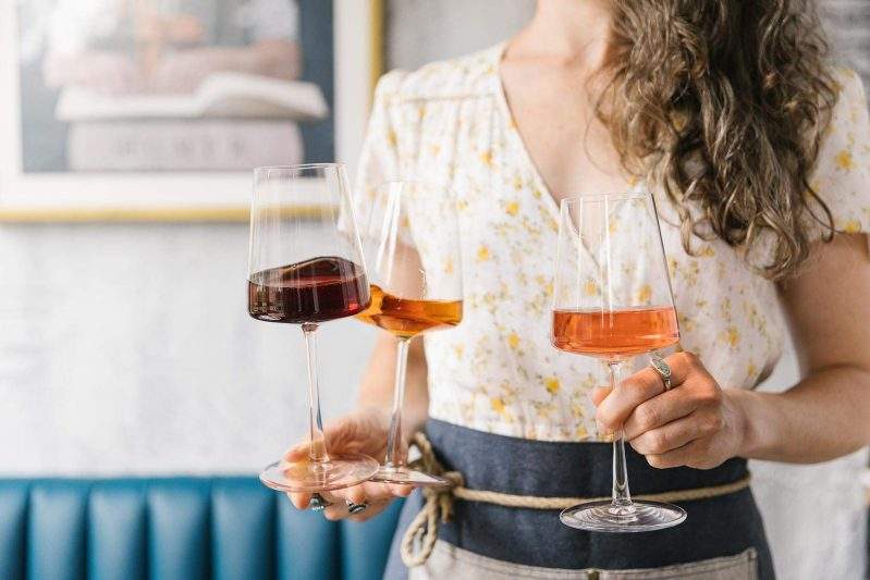 A server holds three glasses of wine at Krasi in Boston