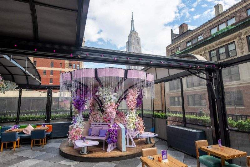 A pink and purple floral installation adorns the outdoor space at Magic Hour Rooftop Bar & Lounge in New York City.