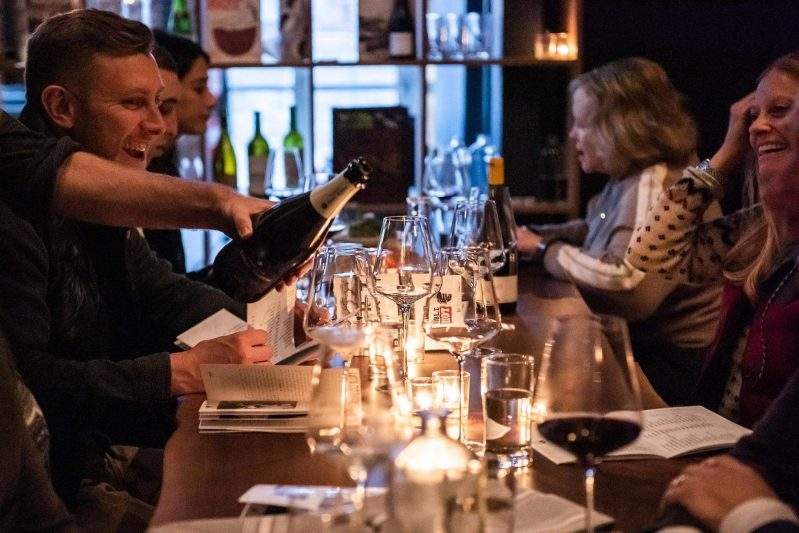 A server pours wine at a bar packed with diners at Noble Riot in Denver