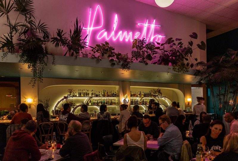 A neon pink sign and plenty of tropical plants adorn the interiors at Palmetto in Oakland