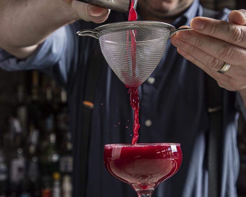 A bartender strains magenta-colored juice into a coupe glass at Prohibition in Charleston.