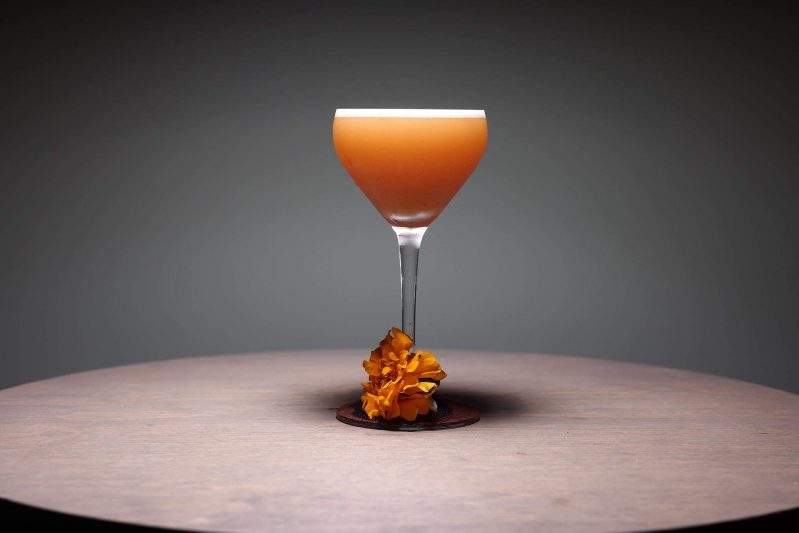 A orange-colored cocktail with a flower on the glass’s stem at Sushi Sato in San Francisco