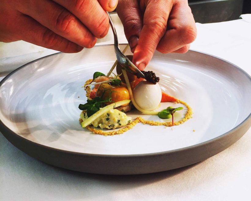 Two hands plating food on a white plate