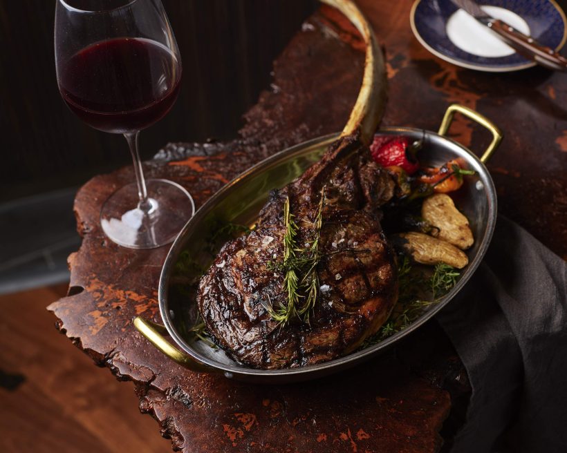 A steak placed on an oval plate next to a glass of red wine at the Dallas restaurant Crown Block.