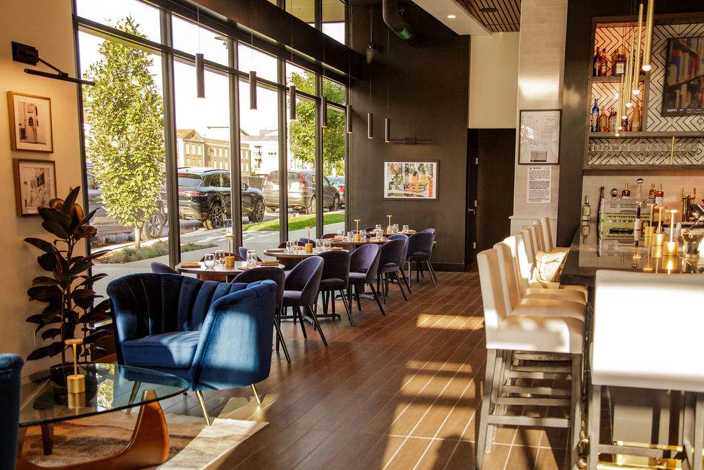 Velvet seats and gold light fixtures surround the bar area at Le French 9&Co in Denver