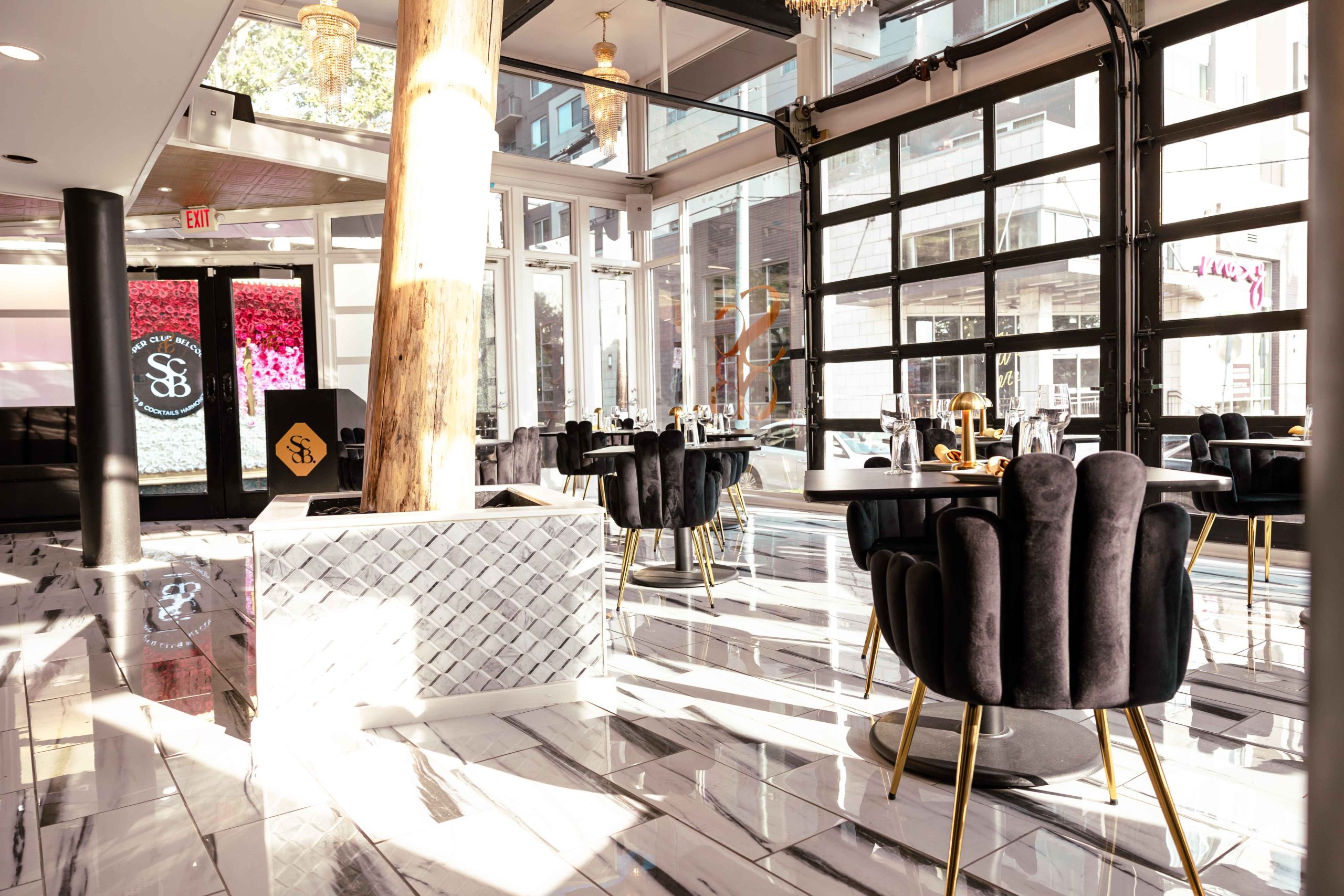 Floor-to-ceiling glass windows, black velvet seats, and gold accents at the Art Deco-inspired dining room at Supper Club on Belcourt
