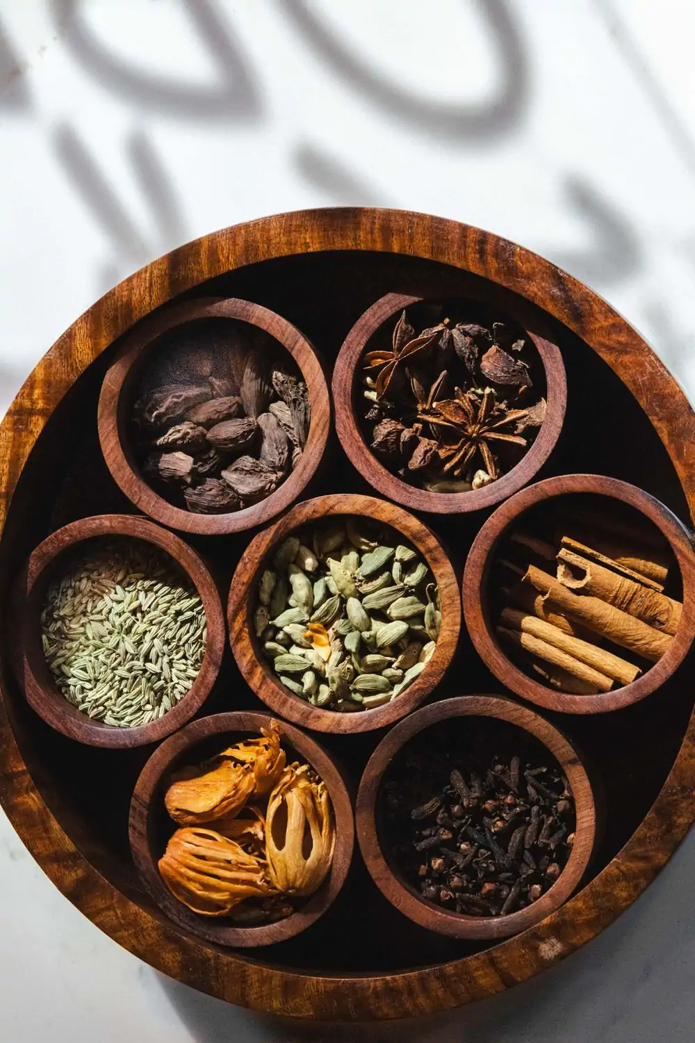 An overhead view of spices displayed in wooden compartments found in traditional Indian dishes, including cinnamon, clove, cardamom, cumin, and anise. These are the spices found in dishes at Rishtedar, one of the best restaurants in Wynwood, Miami.