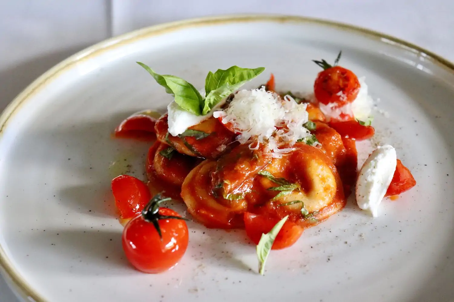 A plate of housemade ravioli in tomato sauce at dōma, one of the best restaurants in Wynwood Miami, topped with basil, grated cheese, ricotta, and cherry tomatoes on a white ceramic dish.