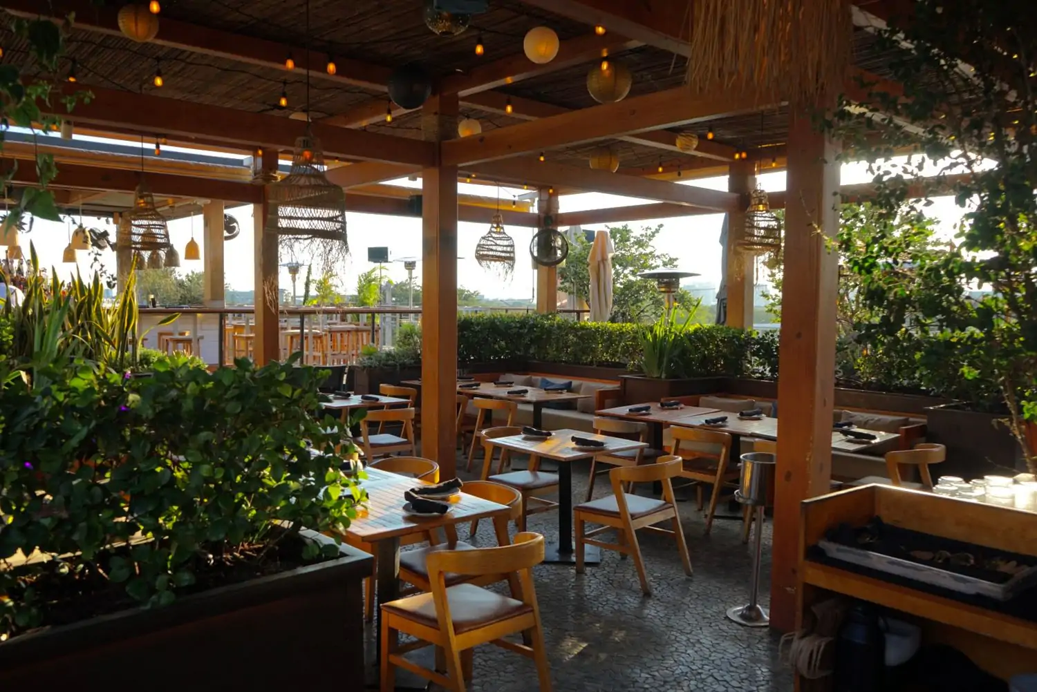 A view of the outdoor rooftop dining area at Astra, one of the best restaurants in Wynwood, Miami. The dining area has wooden chairs and tables surrounded by greenery.