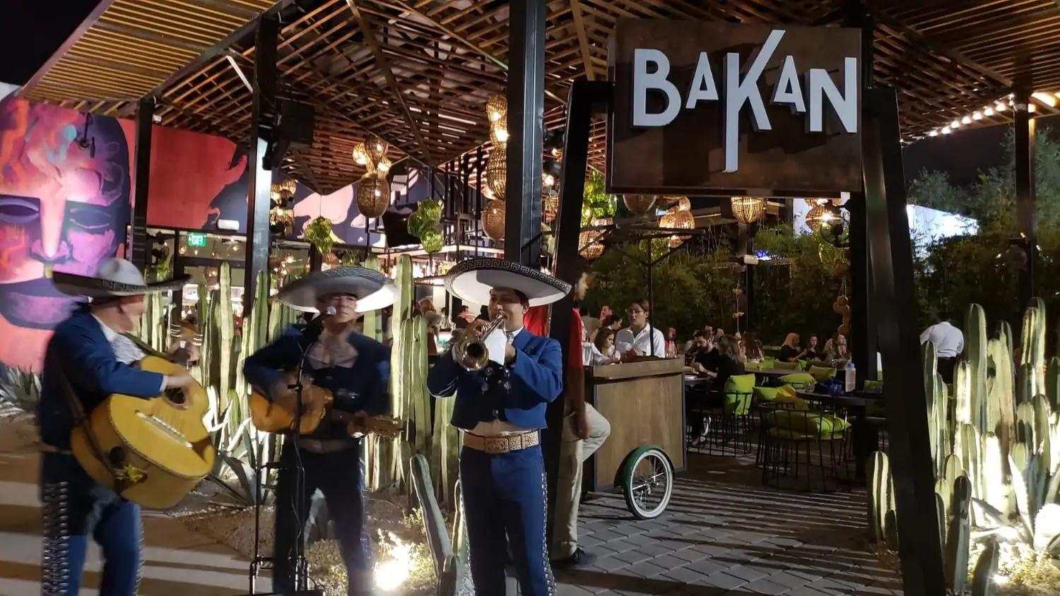 A photo of a mariachi band playing on the patio at Bakan, one of the best restaurants in Wynwood, Miami, available on OpenTable. The outdoor dining area has wood accents, colorful murals, and cactus decorations.