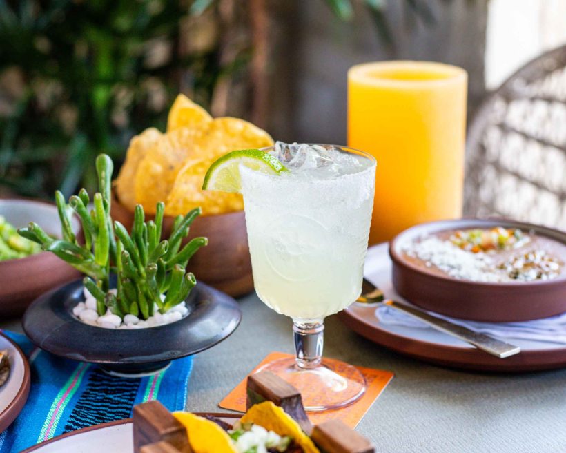 A table topped with a decorative succulent, orange candle, margarita, tortilla chips, and assorted Mexican plates at Bulevar Mexican Kitchen in Austin