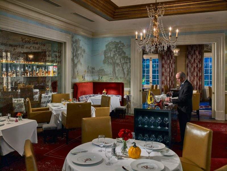 A server pours wine into a glass carafe in the velvet-heavy dining room at Restaurant R’evolution in New Orleans.