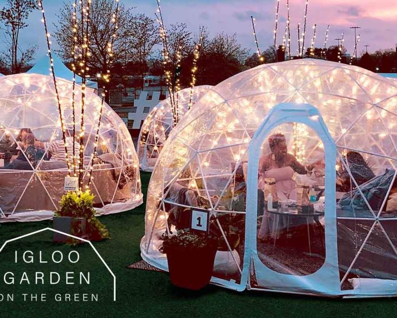People dining inside heated and lighted igloos with trees in the background