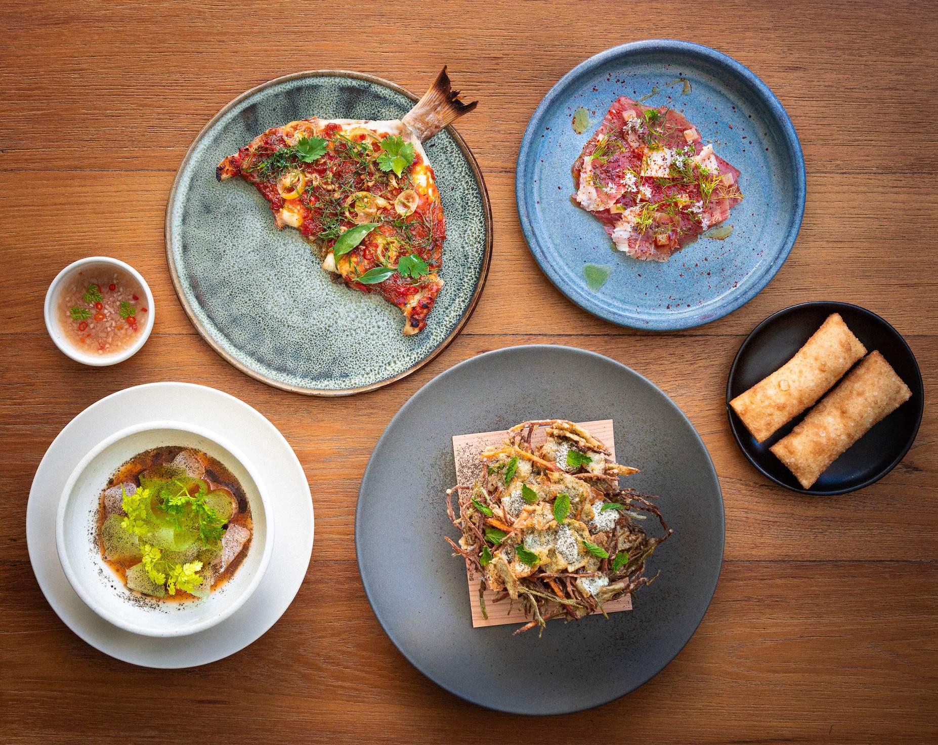 Various food dishes shown side by side on a wooden table at the Los Angeles restaurant Gunsmoke