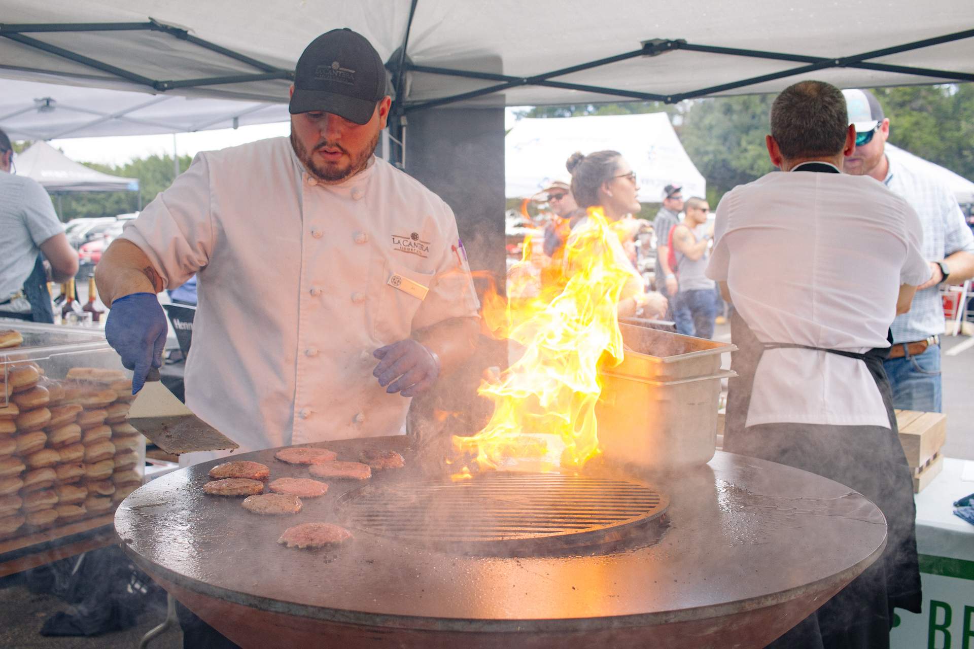 A chef prepares some burgers next to an open flame at the food festival Tasting Texas